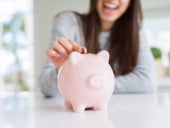 Young woman smiling putting a coin inside piggy bank as savings for investment.