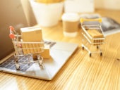 Brown paper boxs in a shopping cart with laptop keyboard on wood table with office background.