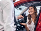 A car sales agent handing out the keys to a brand new car purchased by a happy customer.