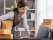 Picture of a merchant woman processing orders while holding boxes.