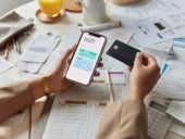 A woman holding her smarthphone and credit card while working on financial documents.